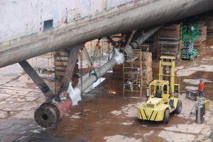 Dry docked ship being repaired by staff with forklift