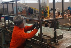 Custom metal fabrication by worker in orange jumpsuit with visor