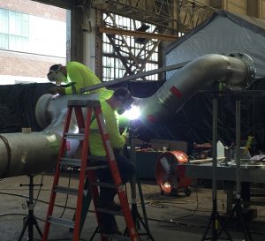 custom metal fabricated piping system being welded by workers